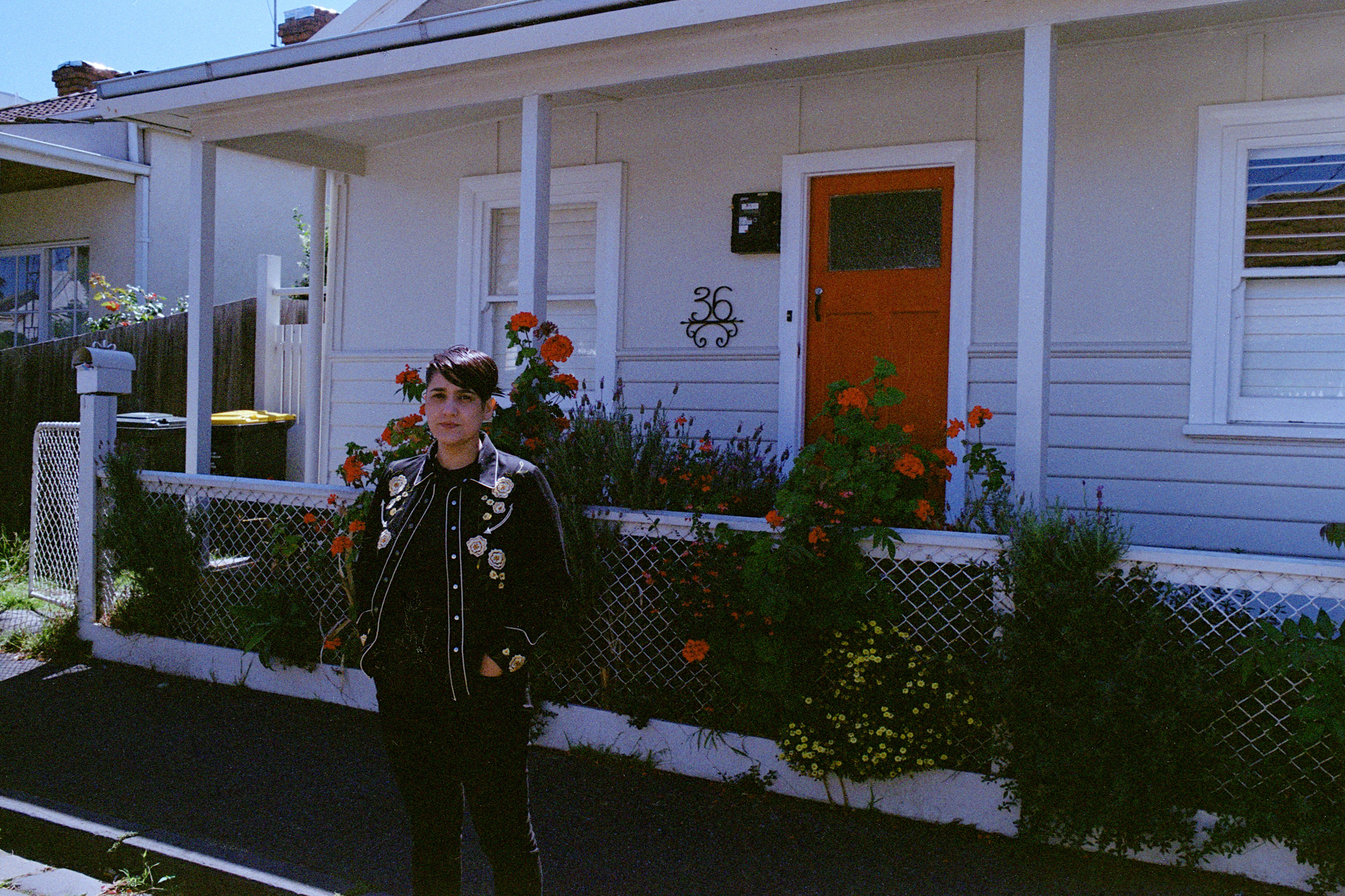 Person standing in from of house with a red door and red flowers.